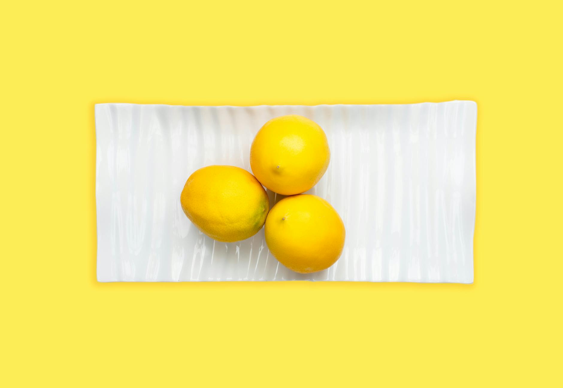 Fresh lemons arranged on a white plate with bright yellow background