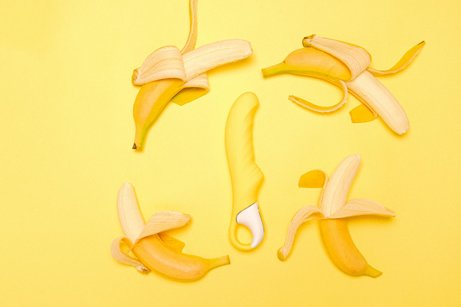 A yellow silicone lemon vibrator surrounded by peeled bananas on a bright yellow background