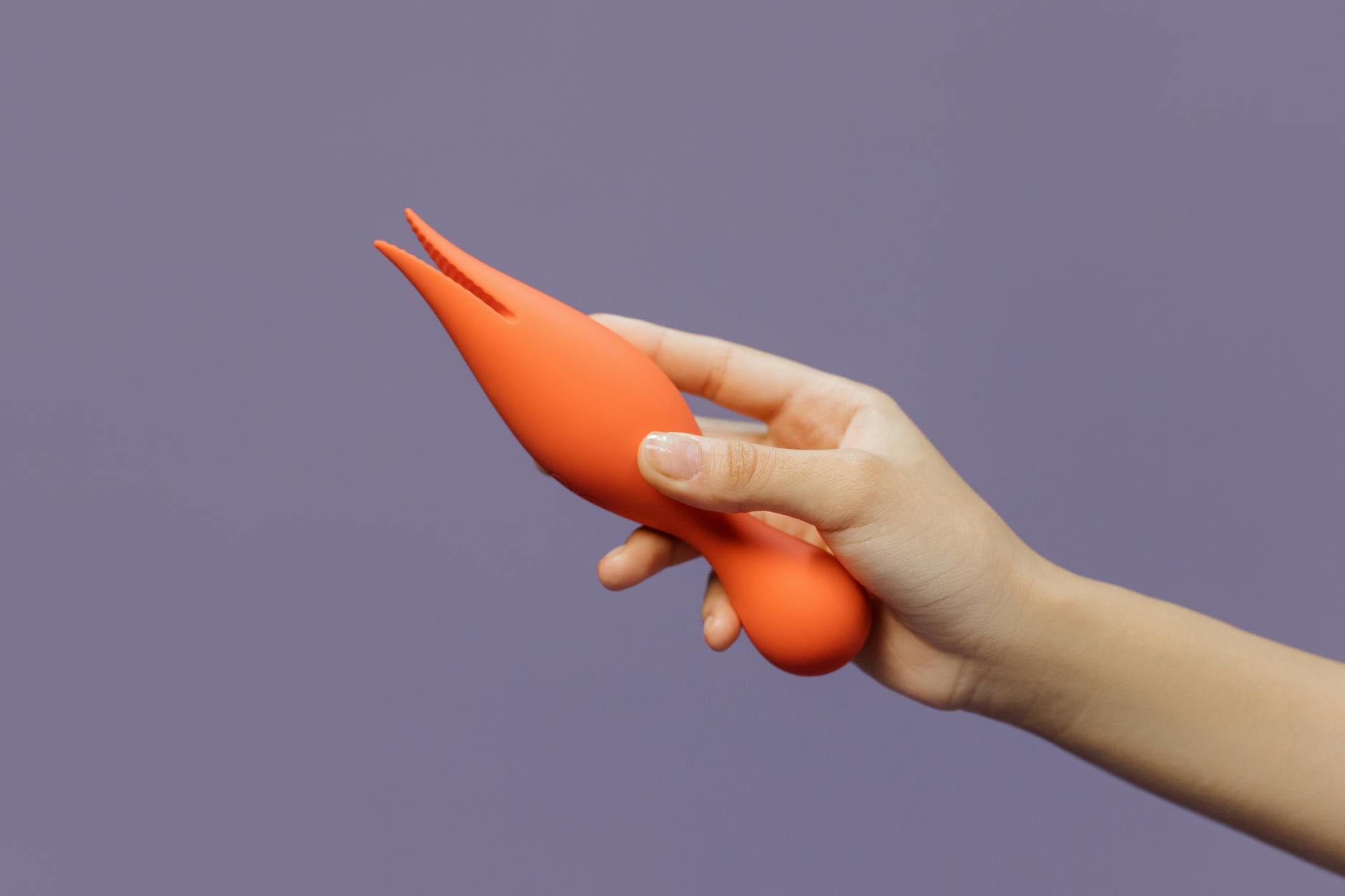 A hand holding an orange vibrator against a minimalistic purple backdrop, showcasing modern sensuality and intimate communication