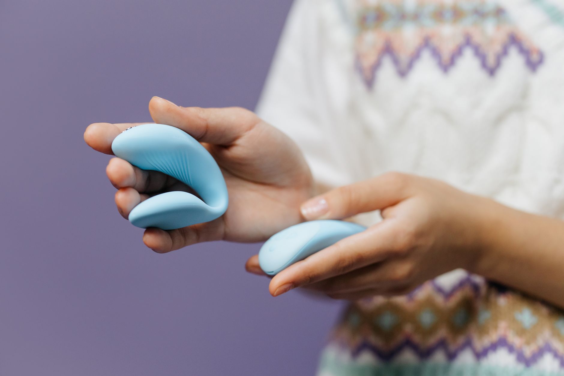 Eine Hand hält einen eleganten blauen Lemon Vibrator gegen einen violetten Hintergrund