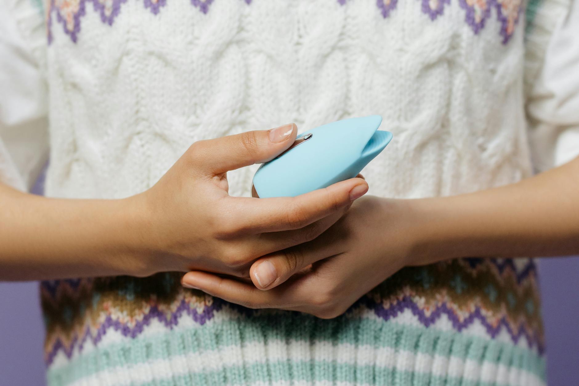 Close-up of hands holding a blue personal massager, showing gentle touch and calm presence.