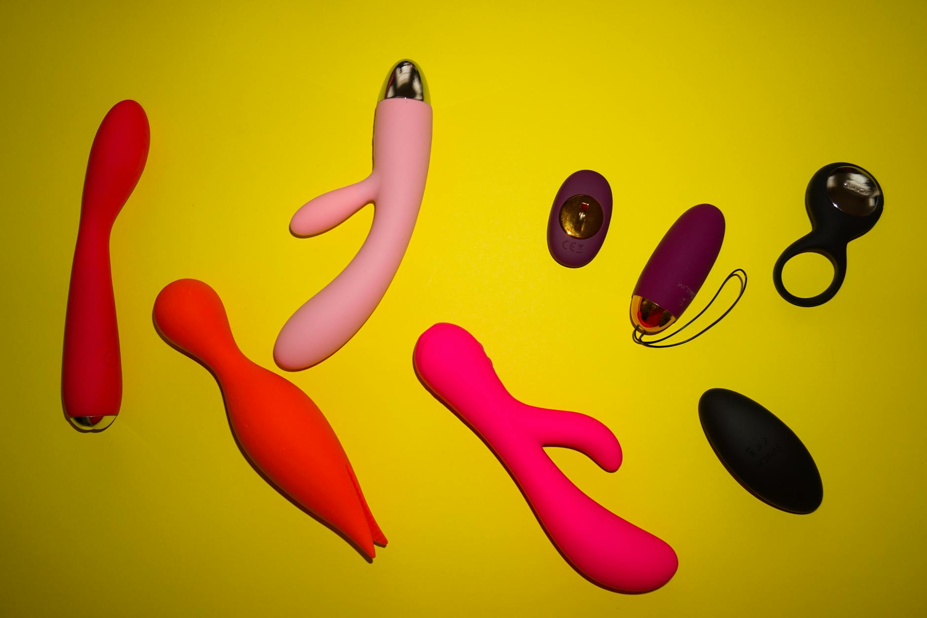 Vibrant array of colorful sexual toys arranged on a bright yellow surface, showing various designs and styles for pleasure